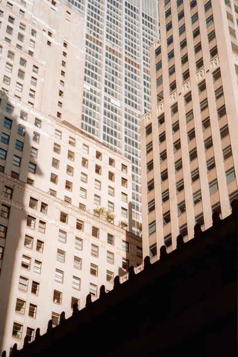 Sunlight illuminates the facades of several tall buildings, with a dark, ornate structure in the foreground.