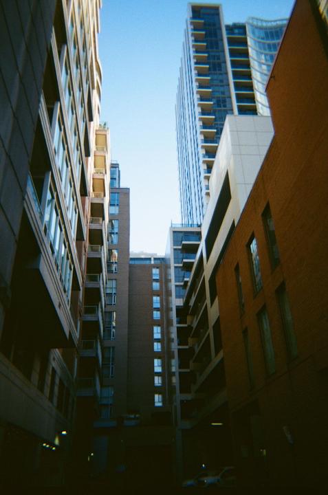 A low-angle view shows tall buildings with many windows and balconies, with a bright blue sky above.