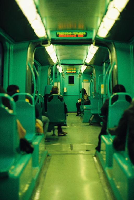 People sit in a green subway car with bright overhead lights.