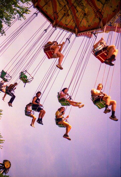 People are riding a swing ride at an amusement park against a purple sky.
