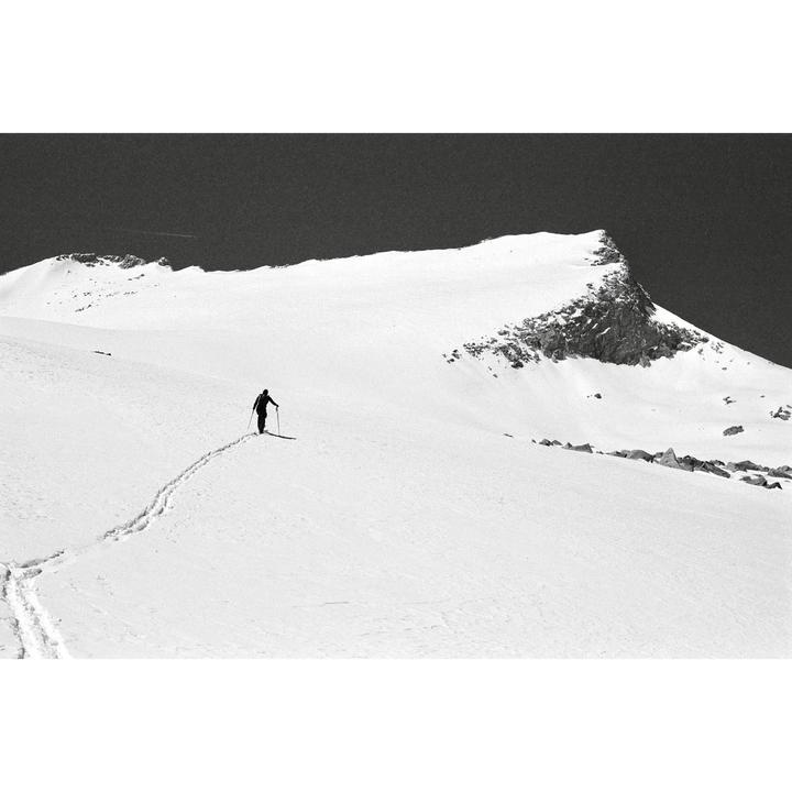 A person skis across a snow-covered mountain with a dark sky above.