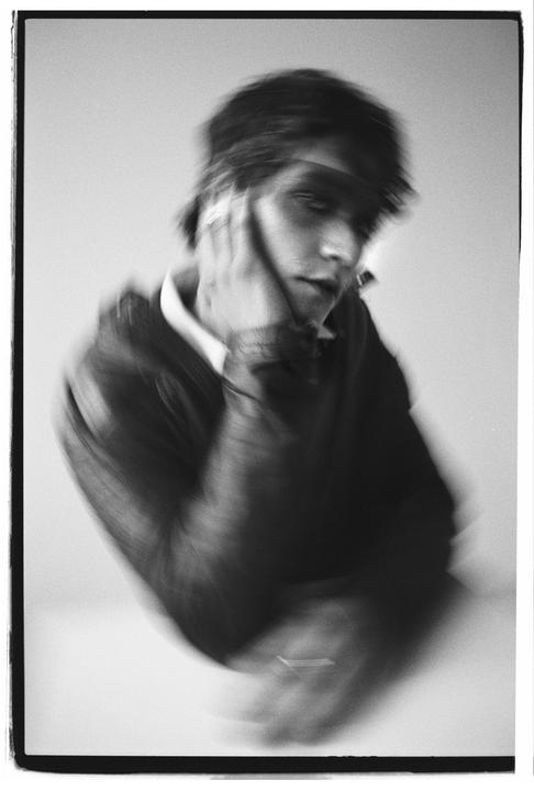 A man with blurred hair and face holds his hand to his cheek.