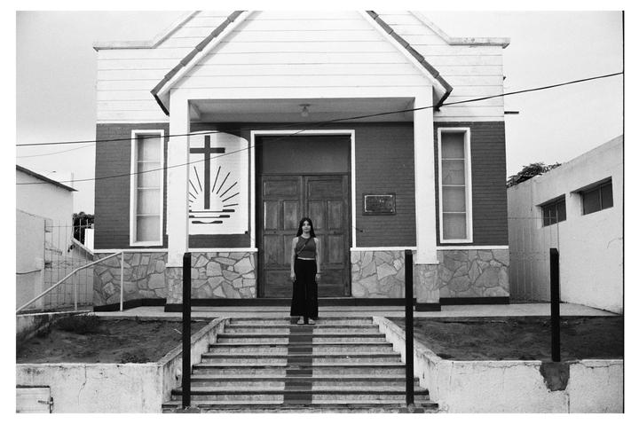 A woman stands at the top of a set of stairs in front of a church with a cross painted on its facade.