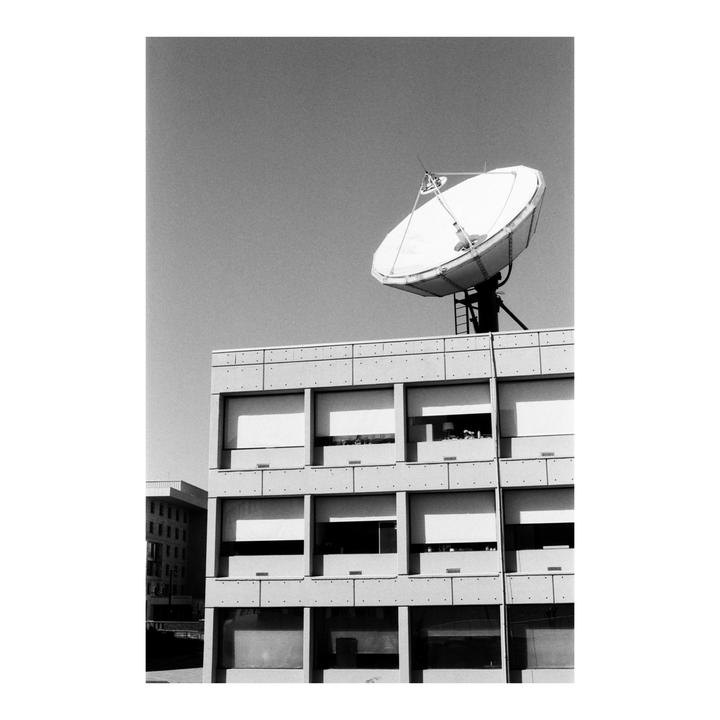 A large satellite dish sits atop a building with many windows, some of which are covered by blinds.