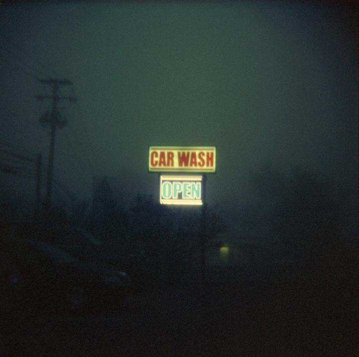 A neon sign for a car wash that says "OPEN" is visible through a thick fog at night.