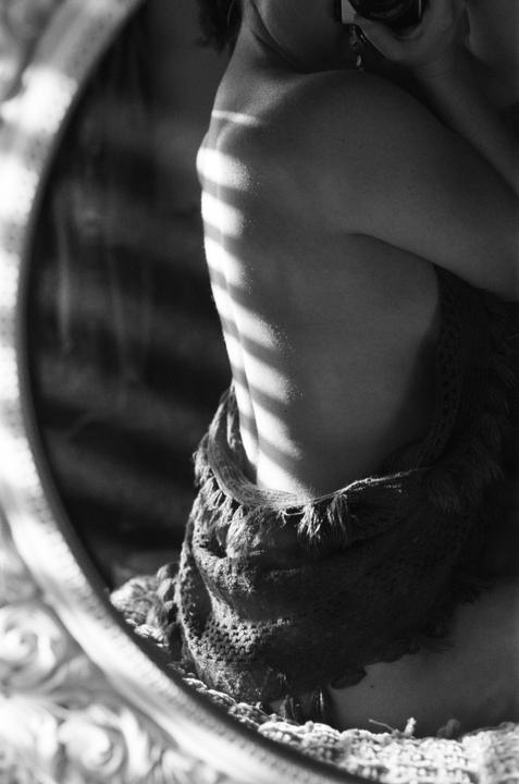 A woman's back is visible in a mirror, with light stripes across her skin.