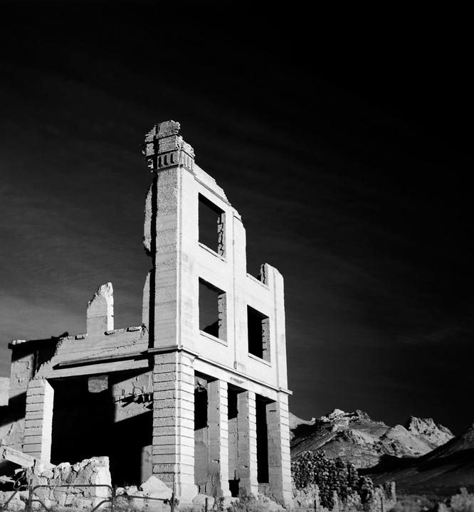 The ruins of a large building stand against a dark sky with mountains in the background.