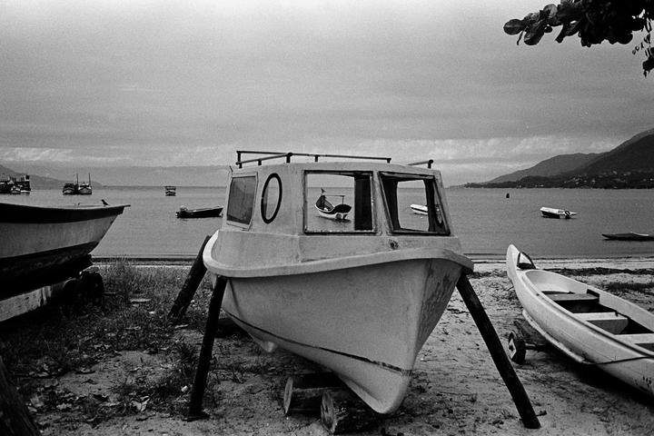 Several boats are visible on a beach and in the water, with mountains in the distance under a cloudy sky.