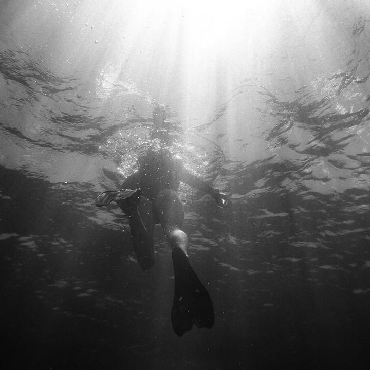 A person wearing fins swims underwater with light rays shining through the surface.