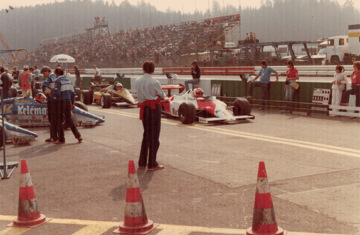 A crowd of spectators watches a Formula 1 race from grandstands overlooking the track.