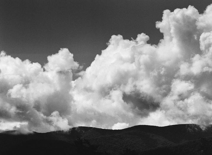 Clouds gather above a dark, tree-covered mountain range.