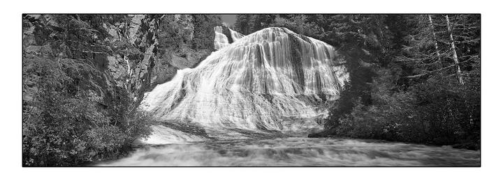 A wide shot shows a waterfall cascading over a rocky cliff into a river, surrounded by dense forest.