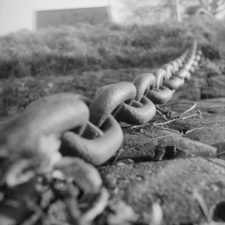 A metal chain stretches across the ground with grass and a building in the background.