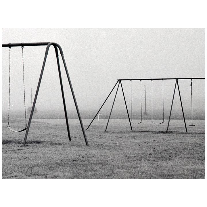 Two swing sets stand on a grassy field under a hazy sky.