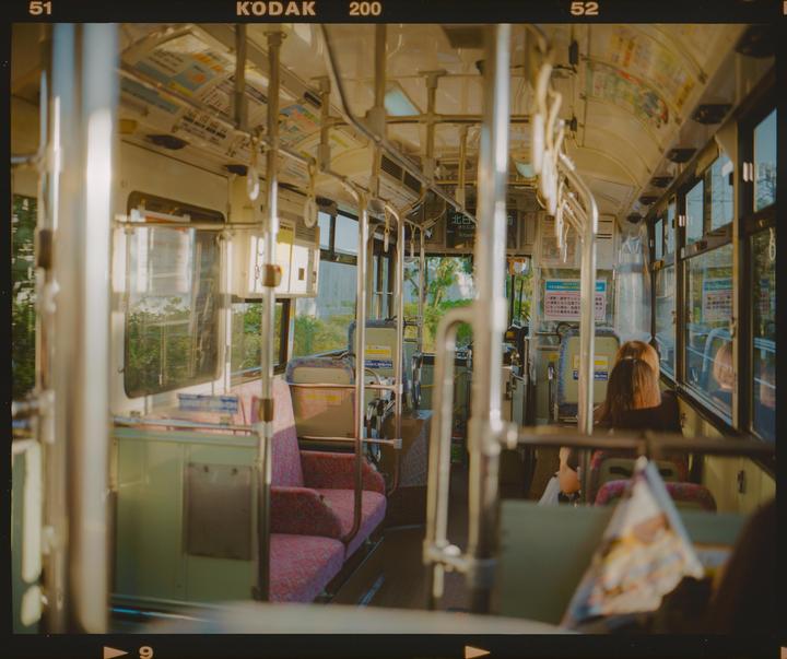 A woman sits on a bus with empty seats and handrails.