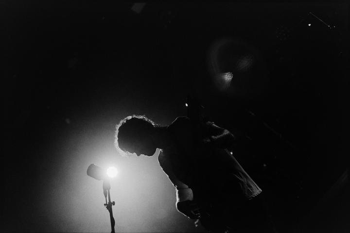 A man is silhouetted against a bright stage light next to a microphone.