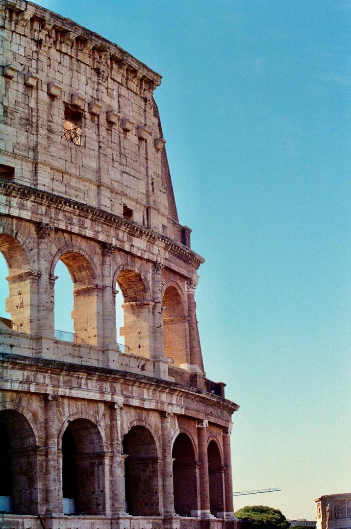 The Colosseum in Rome is visible from a low angle, with a clear blue sky in the background.