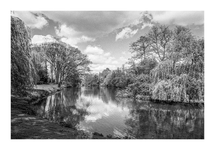 A river flows between grassy banks lined with trees under a cloudy sky.