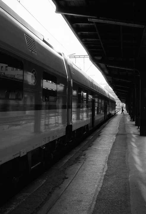 A train is parked at a station platform with a person walking in the distance.