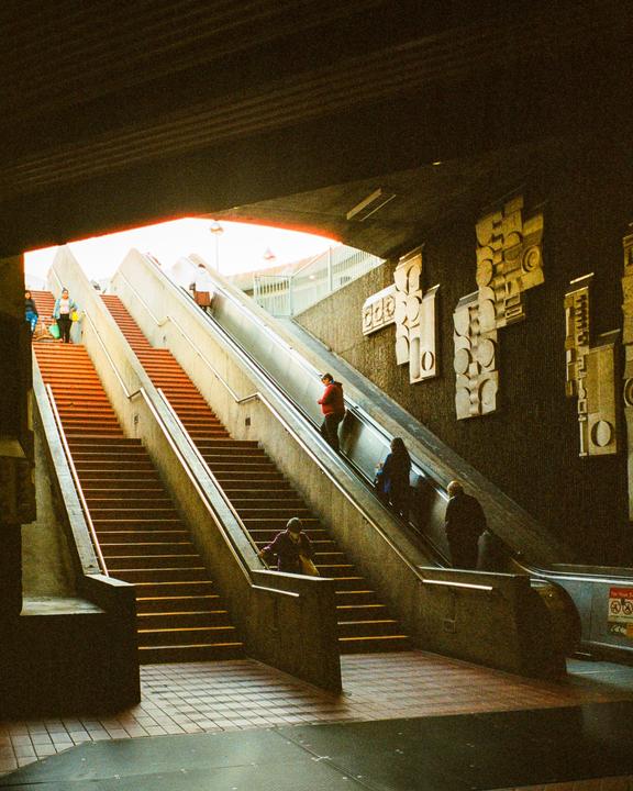 People walk up and down a long set of stairs and escalators at a station exit.