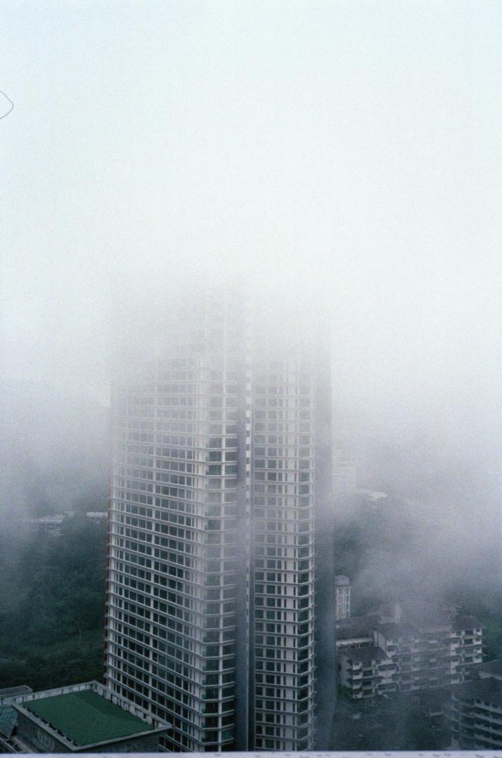 A tall building is partially obscured by fog, with other buildings and trees visible below.