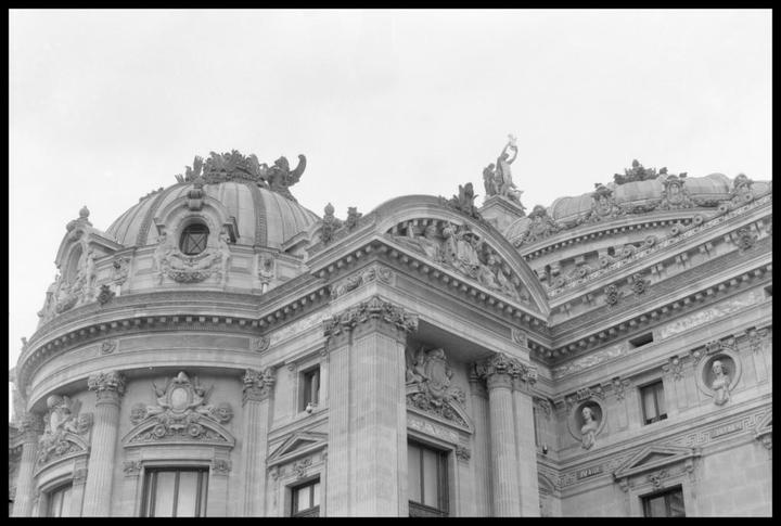 A detailed view of the ornate architecture of a building with a dome and sculptures is shown.