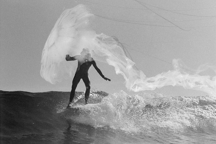 A surfer rides a wave with a large, translucent jellyfish-like object appearing to float above them.