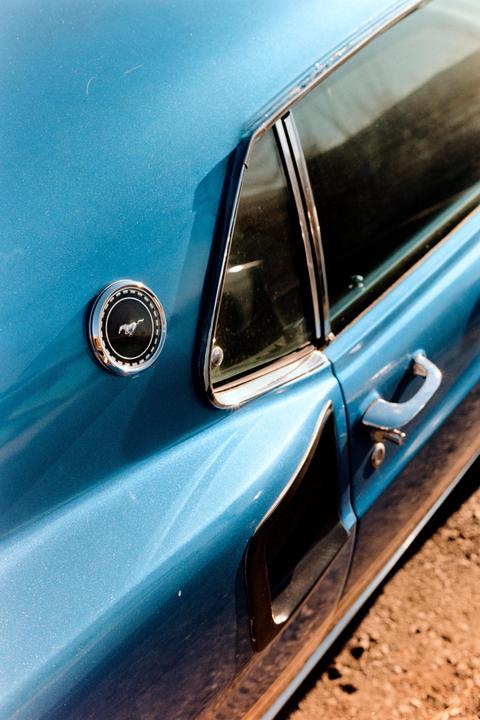 A close-up shot shows the side of a blue vintage car with a mustang emblem, window, and door handle.