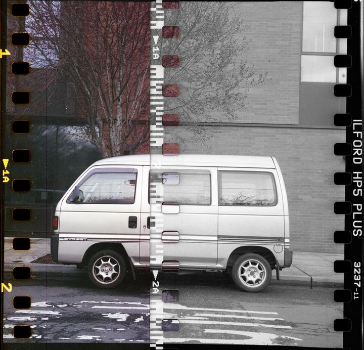 A silver van is parked on a street next to a building and a tree, with the image split between color and monochrome.