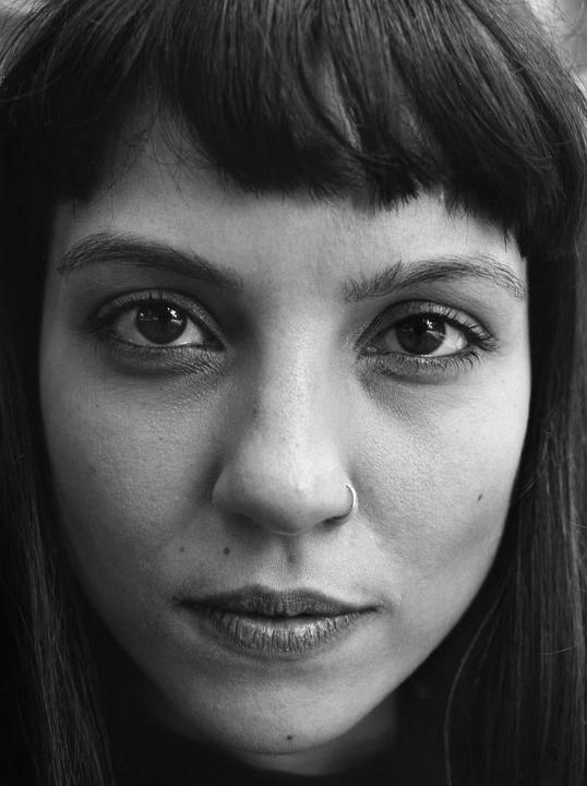 A woman with bangs and a nose ring looks directly at the viewer.