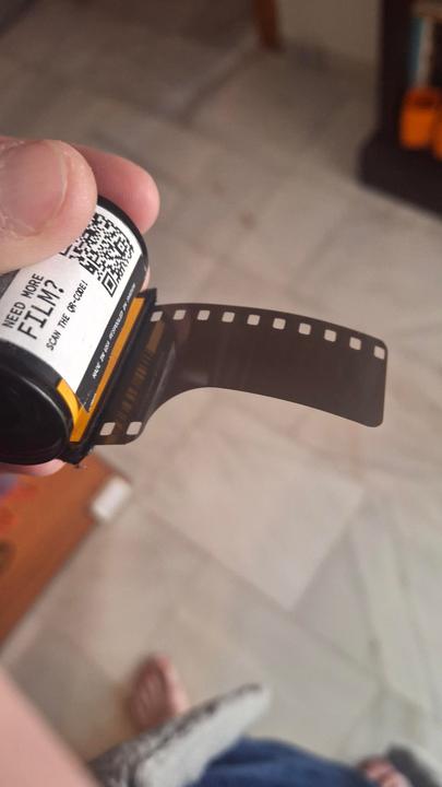 A hand holds a film canister with film partially unspooled from it.
