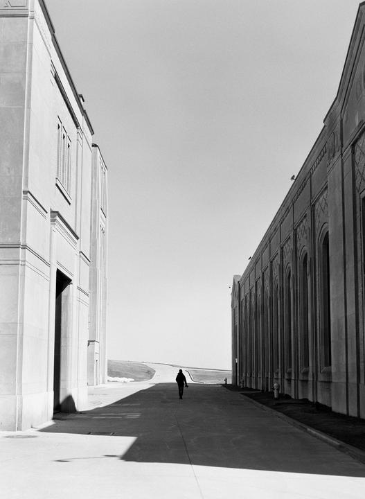 A person walks down a road between two large buildings, with a bright sky overhead.