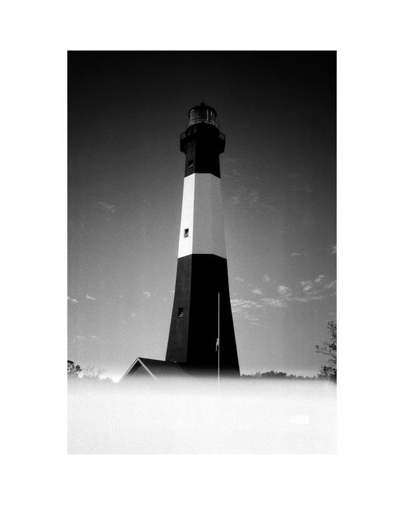 A tall, striped lighthouse stands against a bright sky, partially obscured by fog at its base.