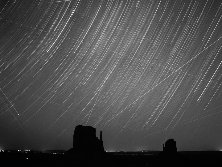 A long exposure photograph shows star trails above the silhouetted rock formations of Monument Valley.