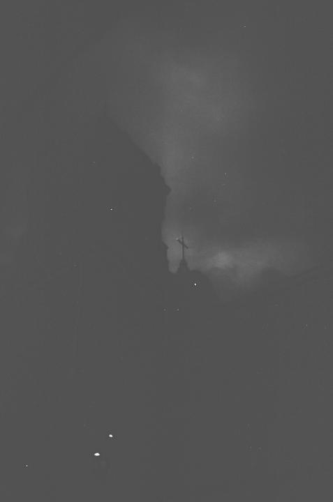 A cross is visible on top of a building against a dark, cloudy sky.