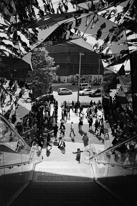 A child runs down a staircase in a busy city street with mirrored reflections of people above.