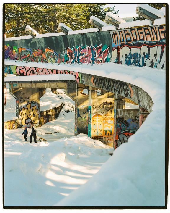 A woman and child walk through a snow-covered bobsled track covered in graffiti.