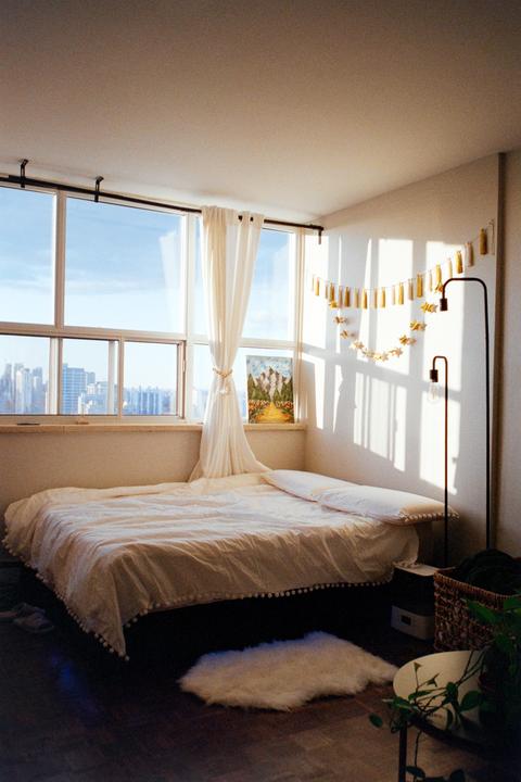 Sunlight streams into a bedroom with a bed, large window, and city view.