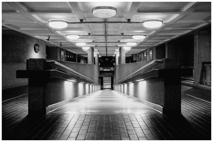 A long, symmetrical hallway with illuminated walls and ceiling lights leads to a dark opening.