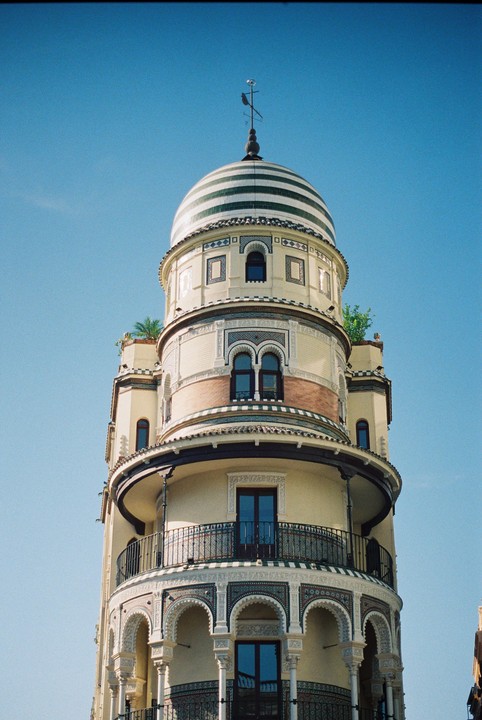 A tall, ornate building with a striped dome and balconies stands against a clear blue sky.