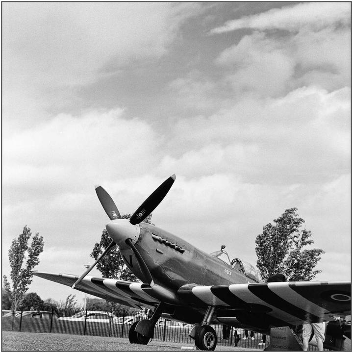 A vintage warplane with a propeller is parked on a grassy field under a cloudy sky.