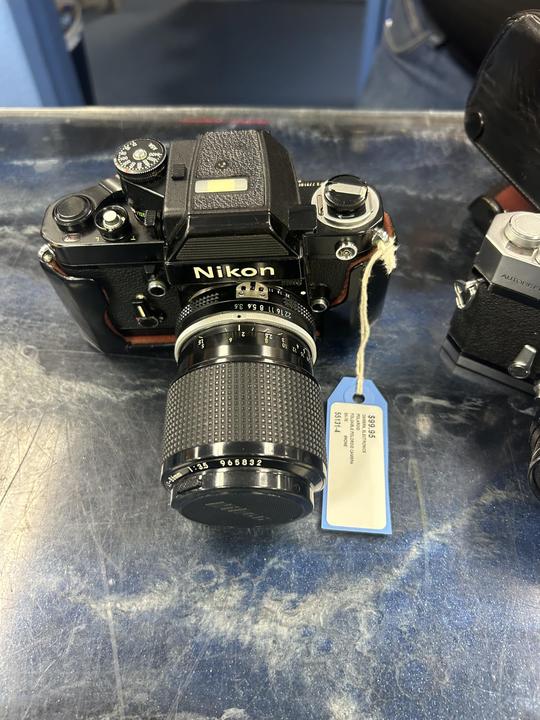 A black camera with a lens and a price tag sits on a blue surface.