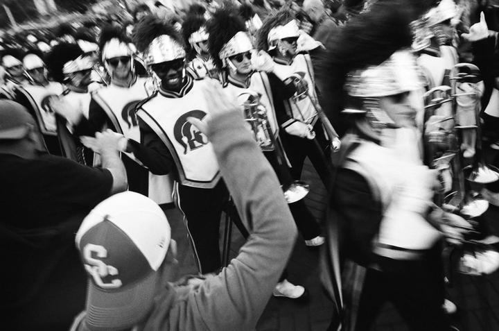A marching band in uniform with instruments is walking past a crowd of people.