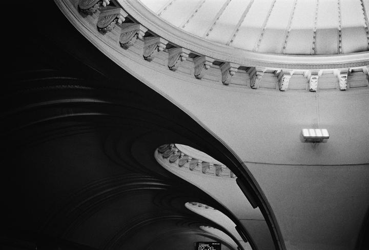 A black and white photo shows the curved architecture of a building interior with decorative elements and a light fixture.