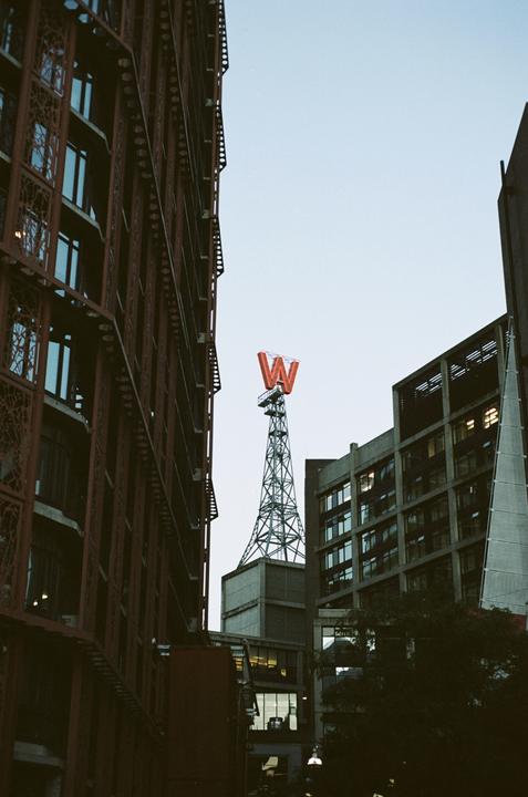 A red letter W sits atop a metal tower surrounded by buildings.