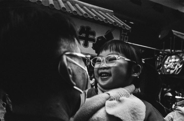 A child wearing glasses laughs while looking at a person wearing a face mask.