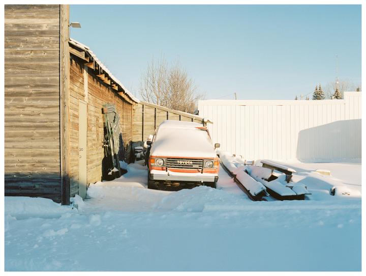 An orange Toyota truck is parked in the snow next to a wooden building.