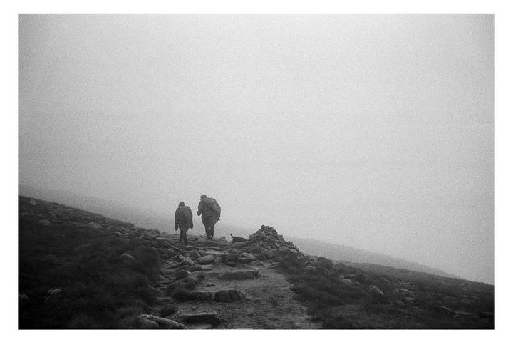 Two people walk up a rocky path on a hazy mountain.