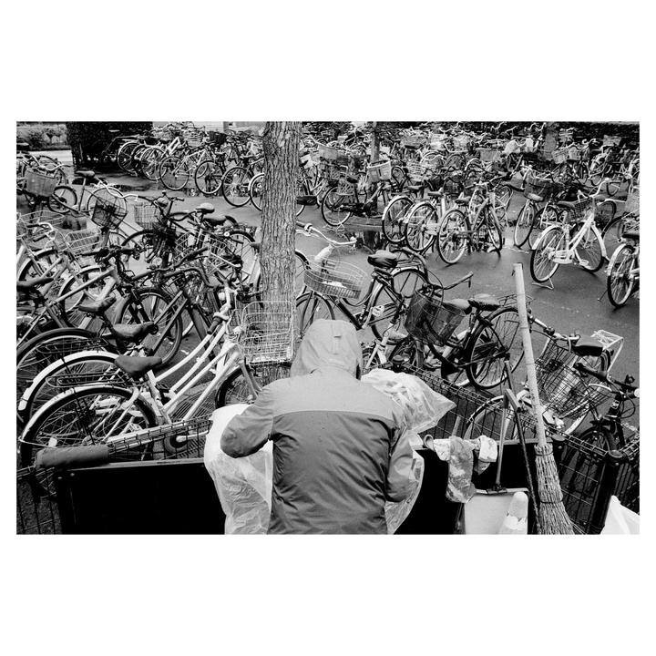 A person in a hooded jacket stands among a dense parking area filled with bicycles.