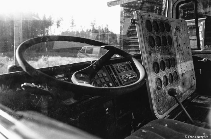 The interior of an old vehicle with a steering wheel and dashboard is illuminated by bright sunlight.